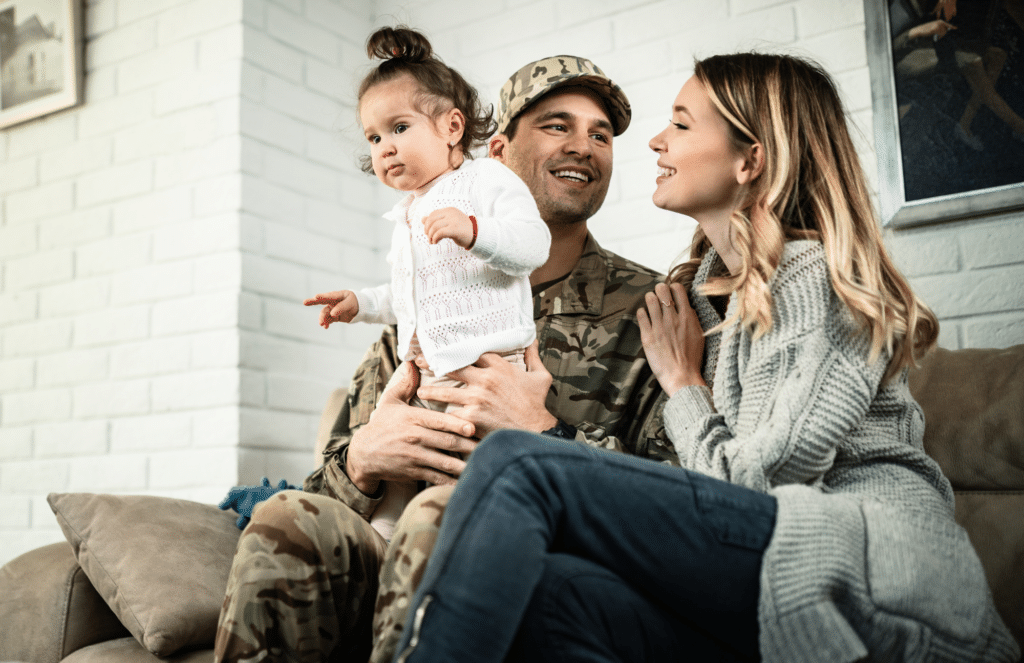 A happy military family smiling together on a couch, representing GEHA dental plan patients at Smile More La Jolla in La Jolla, CA.